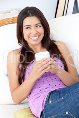 Delighted asian woman holding a cup sitting on the sofa