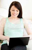 Brunette caucasian teenager using her laptop on the sofa