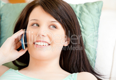 Pretty young woman talking on phone lying on a sofa