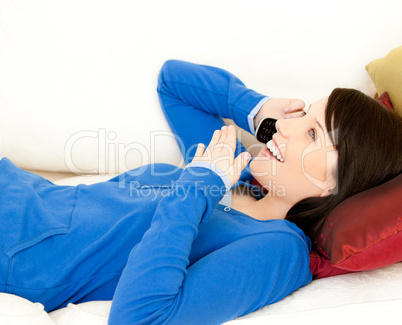 Surprised female teenager talking on phone lying on a sofa