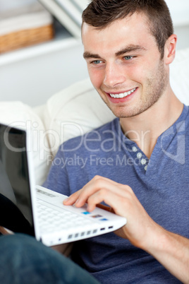 Joyful young man sitting on the sofa using his laptop