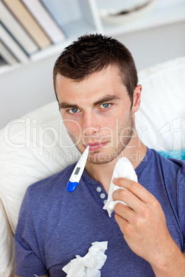 Sick caucasian man sitting on the sofa with thermometer and tiss