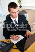 Animated young businessman using his laptop writing on a paper