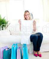 Smiling young woman sitting on the sofa holding a shirt
