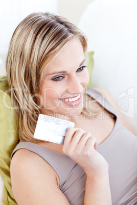 Pretty young woman holding a card sitting on a sofa