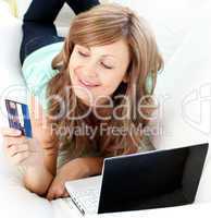 Beautiful woman lying ona sofa holding a card and laptop