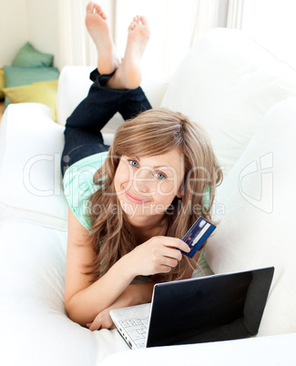 Smiling woman lying ona sofa holding a card and laptop