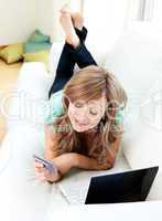 Radiant caucasian woman on the sofa with laptop and card