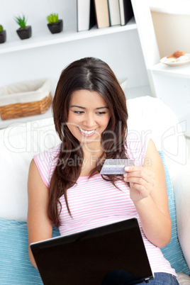 Delighted asian woman using her laptop holding a card