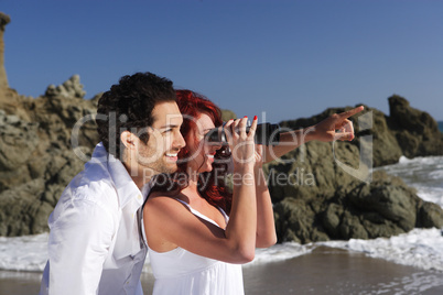 Young Couple at the beach looking through binoculars