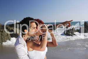 Young Couple at the beach looking through binoculars.