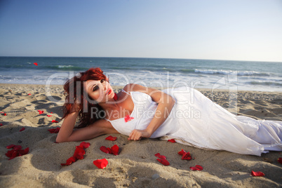 Young woman laying at the beach on sand with rose petals