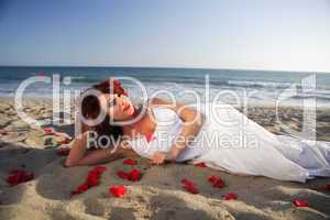 Young woman laying at the beach on sand with rose petals