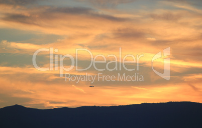 Plane flying upon mountain and clouds by sunset