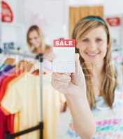 Caucasian blond woman holding a sale paper into the camera