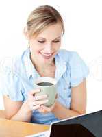 Smiling businesswoman drinking coffee using her laptop