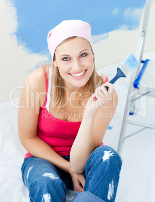 Joyful young woman holding a paint brush smiling at the camera