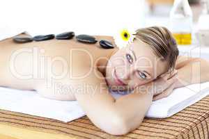 Glowing young woman with hot stone on her back smiling at the ca