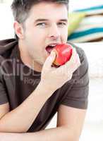 Young man lying on the ground and eating a red apple
