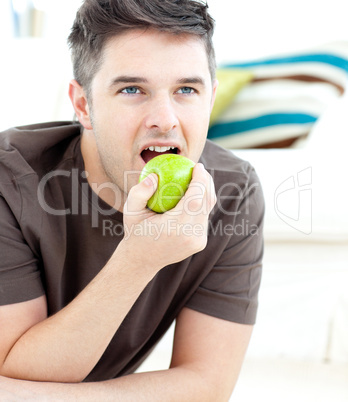 Young man lying on the ground and eating a green apple