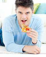 Young man lying on the ground and eating pizza