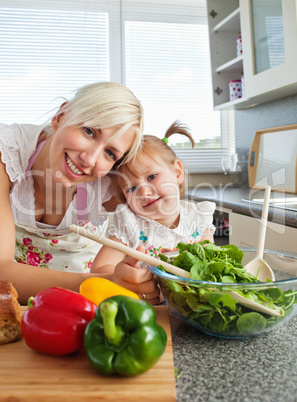Smiling mother and daughter preparing a salad in kitchen