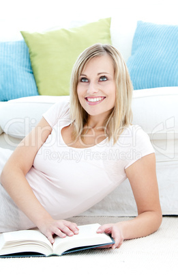 Glowing young woman reading a book on the floor