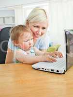 Blond mother and her daughter sitting in front of the laptop