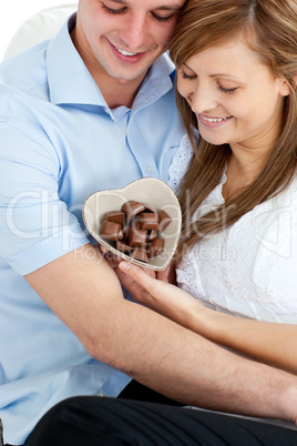 Embracing affectionate couple holding chocolote sitting