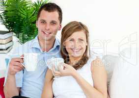Cheerful young couple drinking coffe sitting on a sofa