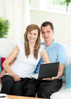 Enthusiastic couple using laptop smiling at the camera