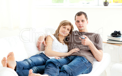 Positive caucasian couple watching tv lying on the sofa