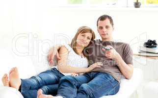 Positive caucasian couple watching tv lying on the sofa