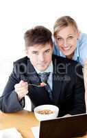 Enamored couple of businesspeople smiling at camera eating cerea