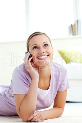 Cheerful young woman talking on phone lying on the floor