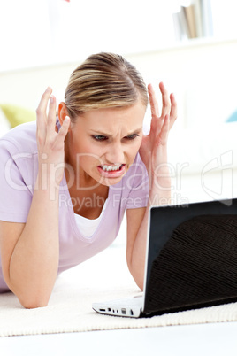 Angry young woman lying on the floor using her laptop