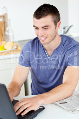 Positive young man using his laptop in the kitchen