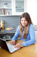 Bright caucasian woman using her laptop in the kitchen