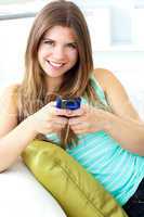 Smiling young woman texting sitting on the sofa