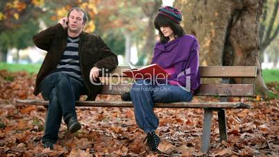 man phoning and girl reading on bench