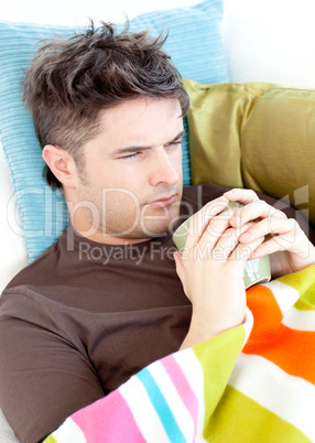 Dejected young man lying on the couch with a hot cup of tea