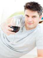 Attractive caucasian man holding a glass of wine lying on the fl