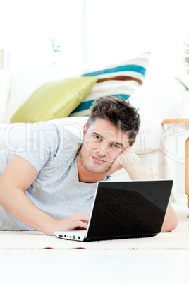 Charismatic young man using his laptop lying on the floor at hom