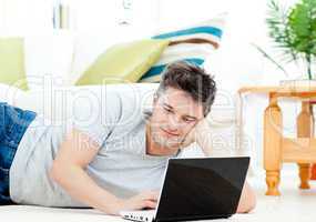 Positive young man using his laptop lying on the floor