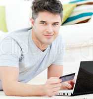 Charming young man holding a card smiling at the camera lying on