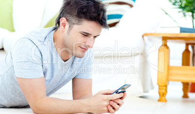Smiling man sending a text lying on the floor