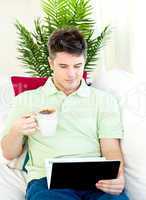 Concentrated young man using his laptop drinking coffee