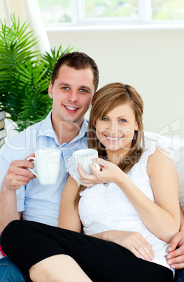 Charming couple holding cups of coffee smiling at the camera