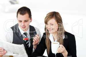 Smiling couple of businesspeople reading the newspaper drinking