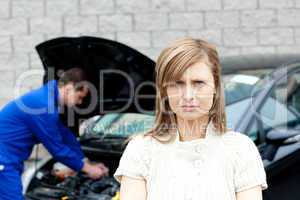 Depressed young woman standing in front of her car